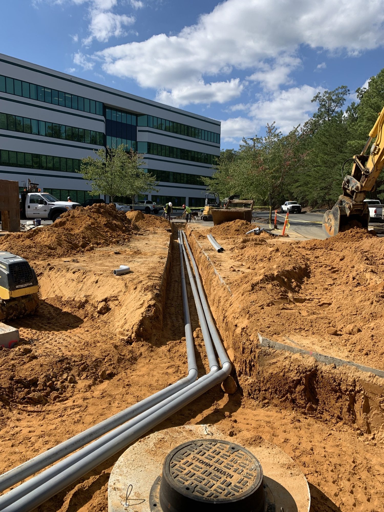 Grouped utility conduits running through an open trench toward a building
