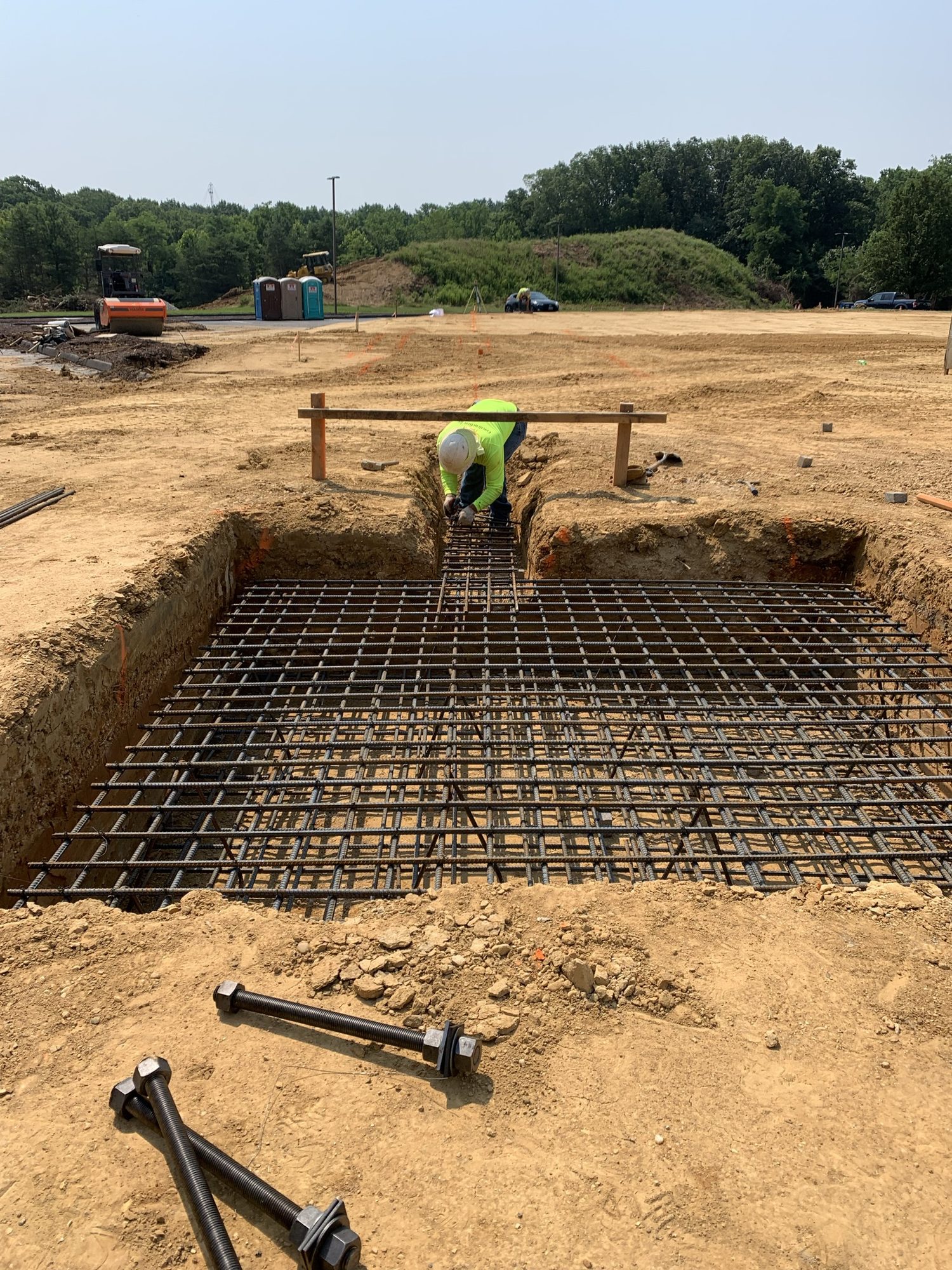 Worker beside reinforcing steel and formwork in an excavated foundation area