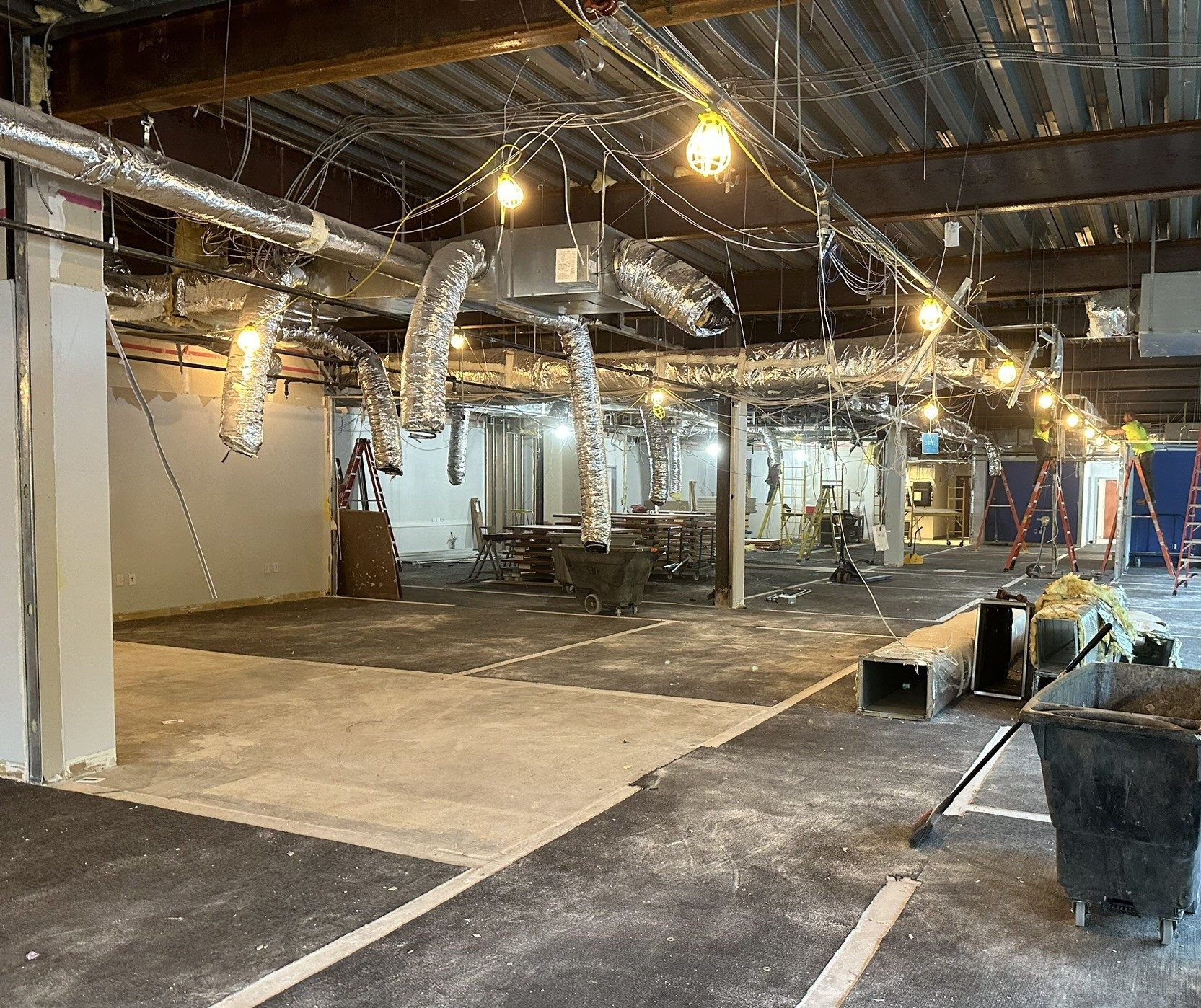 Renovation area with exposed ductwork, temporary lighting, and prepared floor